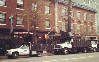 Temporary garbage shoot setup on side of building that drops old roofing materials into trucks waiting below.