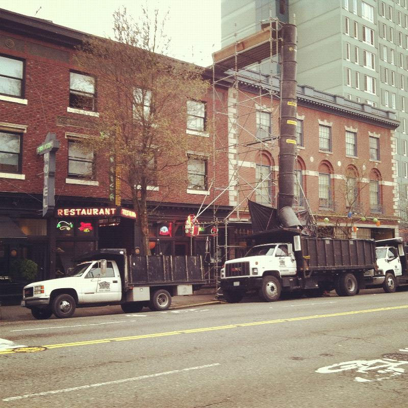 Temporary garbage shoot setup on side of building that drops old roofing materials into trucks waiting below.