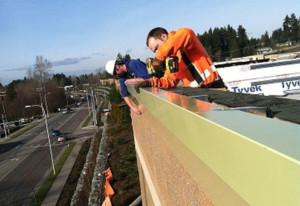 Two roofers drill trimming on the edge of a commercial building.
